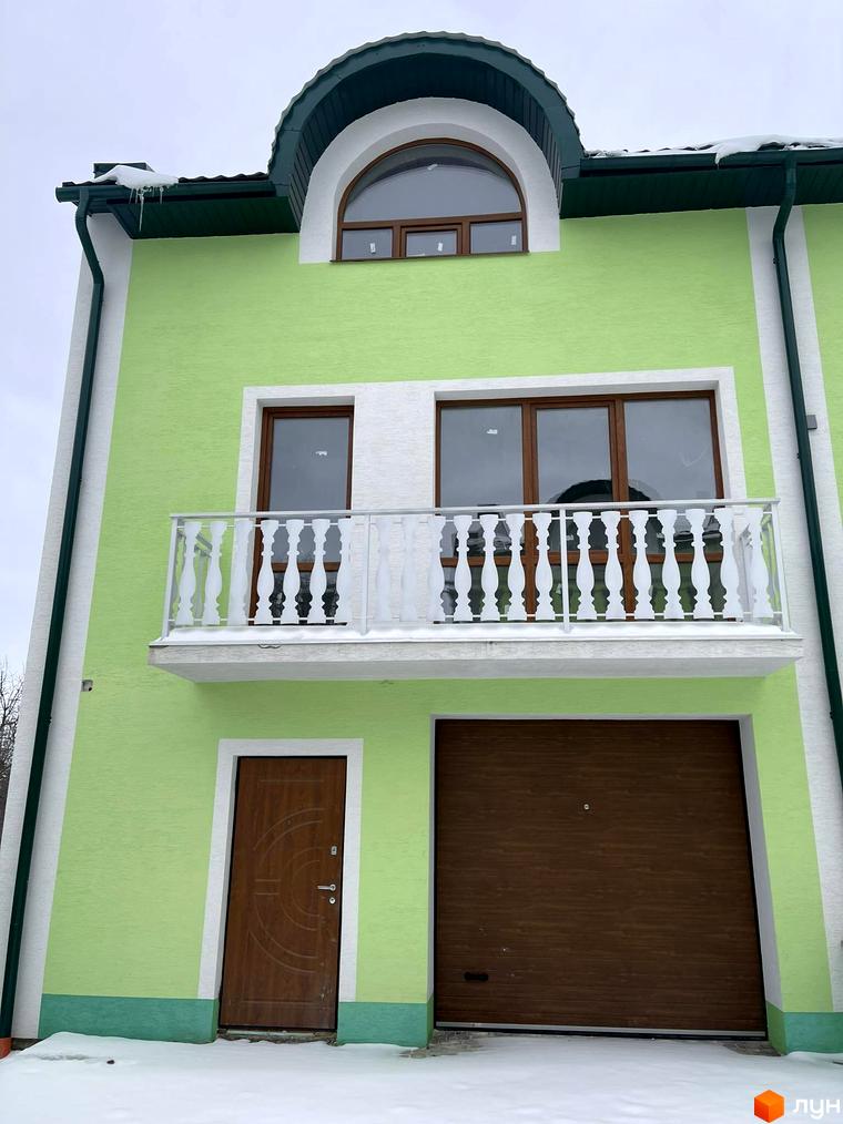 Таунхауси „Гаї Гречинські“: зелений фасад, балкон з білими перилами, дерев'яні двері та гаражні ворота. Зимовий пейзаж з наметами снігу.