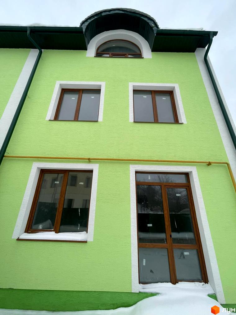 Фасад новобудови Таунхауси „Гаї Гречинські“ з вікнами та дверима. Зелена стіна будинку та сніг біля основи.