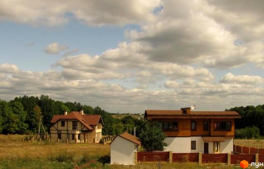 Двоповерховий будинок з коричневою черепицею та світлими стінами. На території є газон, дерева та паркан.