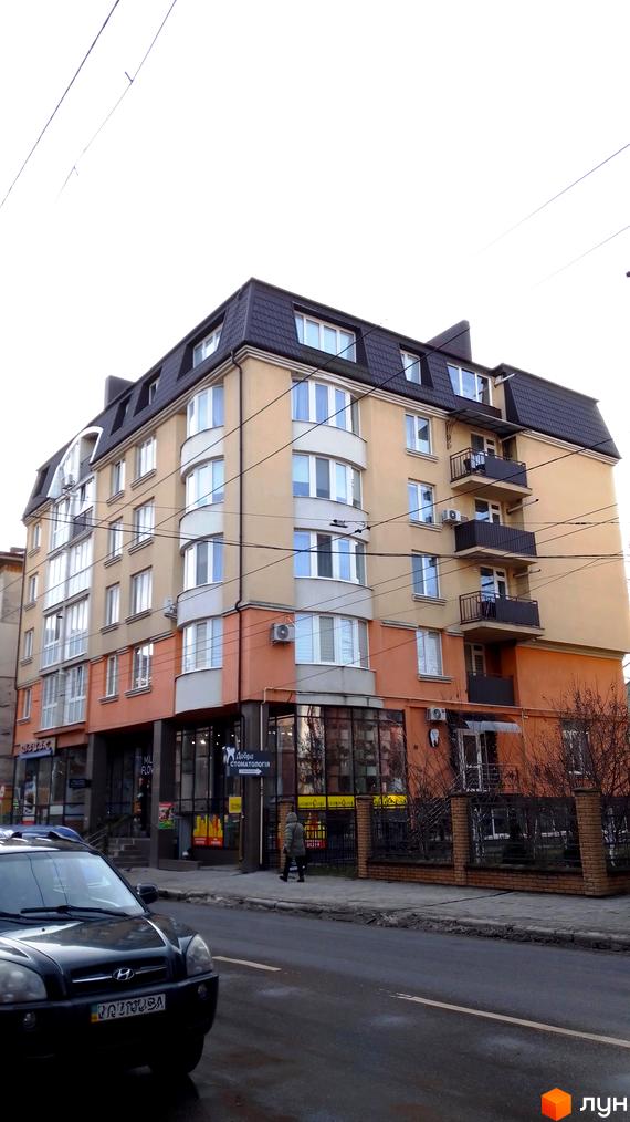 Багатоповерхова новобудова з панорамними вікнами та балконами. На першому поверсі розташовані комерційні приміщення, поруч тротуар та дорога.