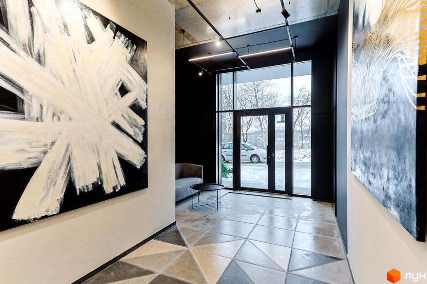 Інтер'єр холу в ЖК ARTHOUSE park з картинами на стінах, скляними дверима та підлогою з геометричним візерунком.