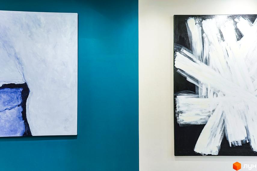Дві картини з абстрактним живописом на стіні в квартирі. Біла стіна, бірюзова стіна, та білі полотна з мазками фарби.