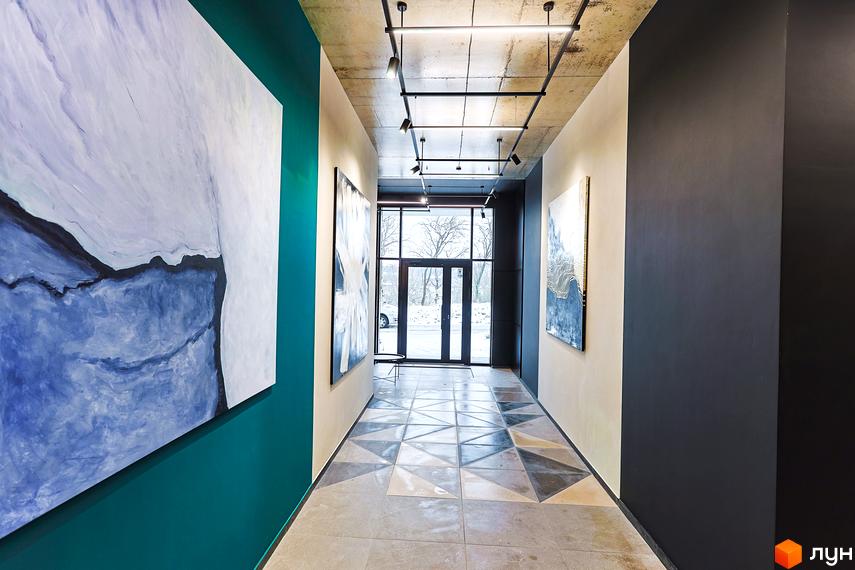 Коридор в ЖК ARTHOUSE park з картинами на стінах, скляними дверима та підсвічуванням. На підлозі плитка з геометричним візерунком.