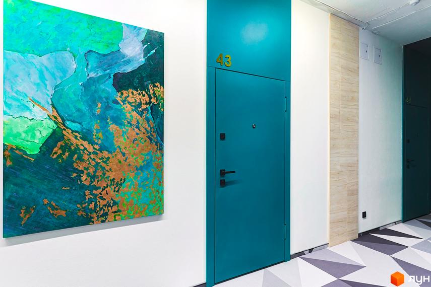 Коридор Житлового комплексу ARTHOUSE park з бірюзовою дверима квартири 43, абстрактною картиною та геометричним візерунком на підлозі.