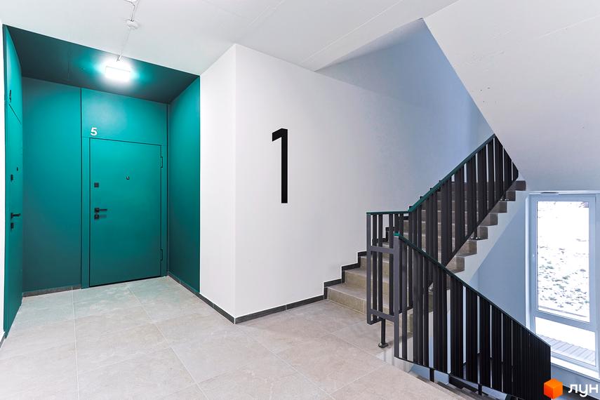Інтер'єр сходової клітки в будинку. Сходи з металевими перилами, стіни білого кольору, двері в коридорі пофарбовані в зелений колір. ЖК ARTHOUSE park.