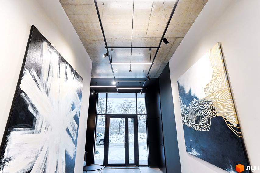 Простора вхідна група Комплексу ARTHOUSE park з панорамними вікнами, крізь які видно засніжену вулицю та дерева. Інтер'єр прикрашений картинами.