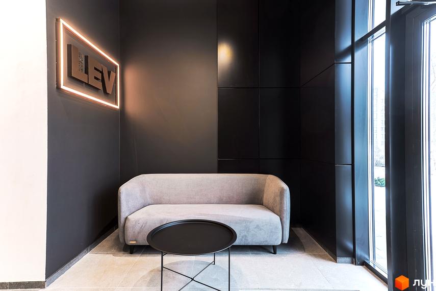 Інтер'єр зони відпочинку в новобудові. Сірий диван, чорний столик та стіни. На стіні вивіска з назвою ЖК ARTHOUSE park.