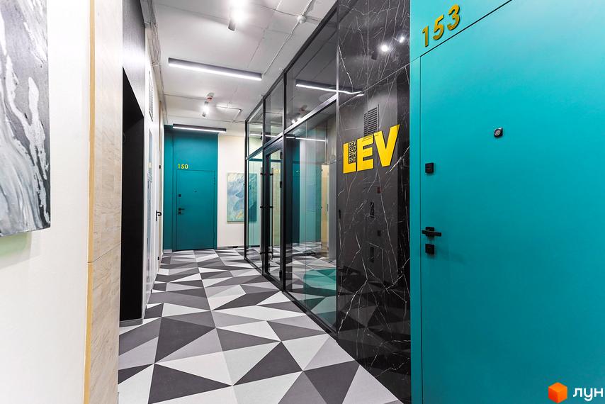 Коридор в новобудові ЖК ARTHOUSE park з дверима бірюзового кольору, геометричною підлогою та скляними перегородками. На стіні логотип забудовника.