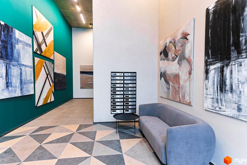 Холл житлового комплексу з картинами на стінах, диваном та столиком. Підлога викладена геометричною плиткою, на стіні розміщені поштові скриньки.