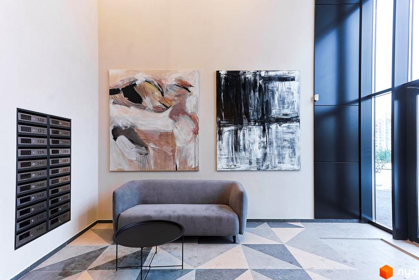 Вестибюль житлового комплексу ARTHOUSE park з картинами на стінах, диваном та столиком. На стіні розташовані поштові скриньки, а поруч - велике вікно.