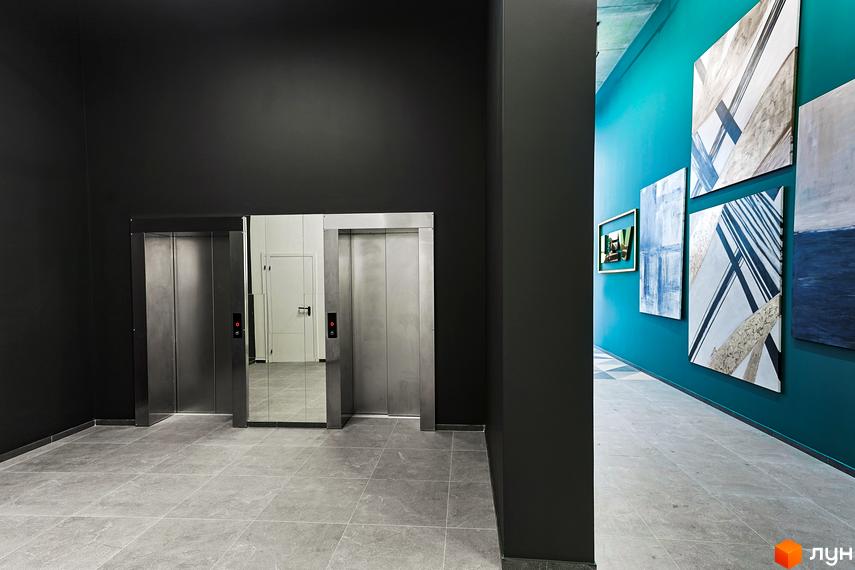 Інтер'єр ЖК ARTHOUSE park з ліфтами та картинами на стінах. Сіра плитка на підлозі, темні стіни та дзеркало.