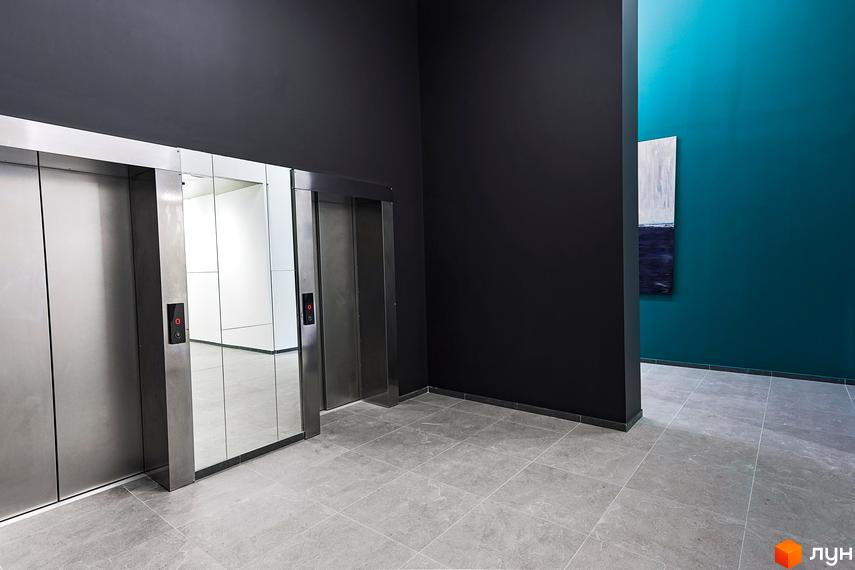 Ліфти в холі ЖК ARTHOUSE park з темними стінами та картиною на фоні. Сіра плитка на підлозі, дзеркальні двері ліфтів.
