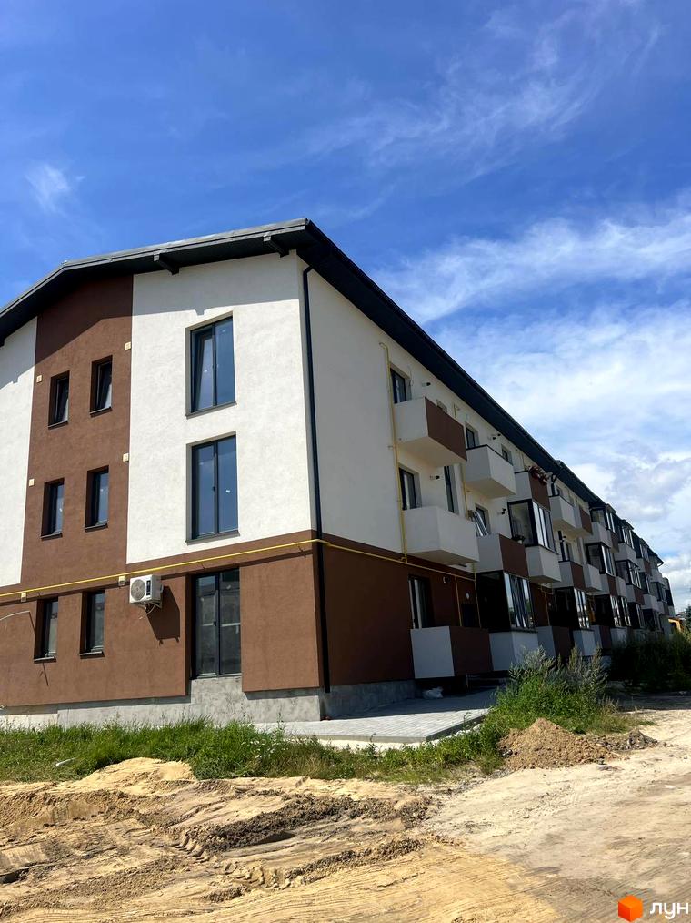 Новобудова Тарас Шевченко з біло-коричневим фасадом та балконами. Навколо будинку видно ділянку з ґрунтом та травою.