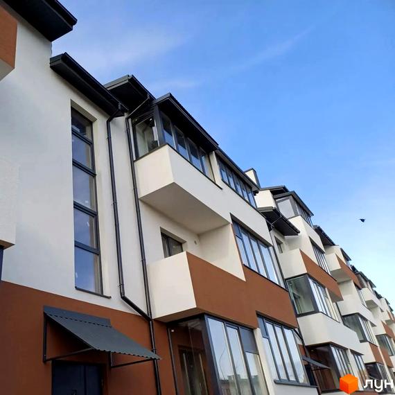 Фасад житлового комплексу Тарас Шевченко з білими та коричневими елементами, великими вікнами та балконами на тлі блакитного неба.