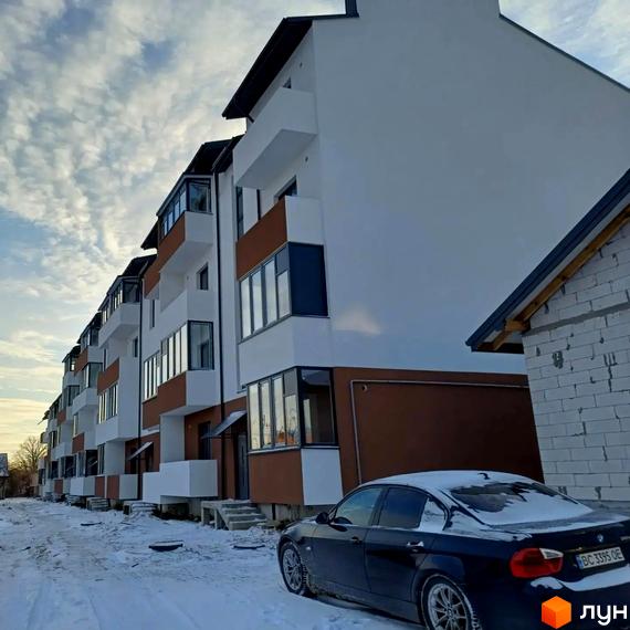 Будинок ЖК Тарас Шевченко з білим фасадом та коричневими елементами, засніжена прибудинкова територія з автомобілем.