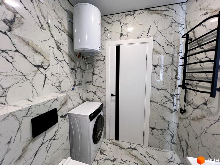 Дизайн ванної кімнати в клубному будинку Васильченка з пральною машиною та бойлером на фоні мармурової плитки.
