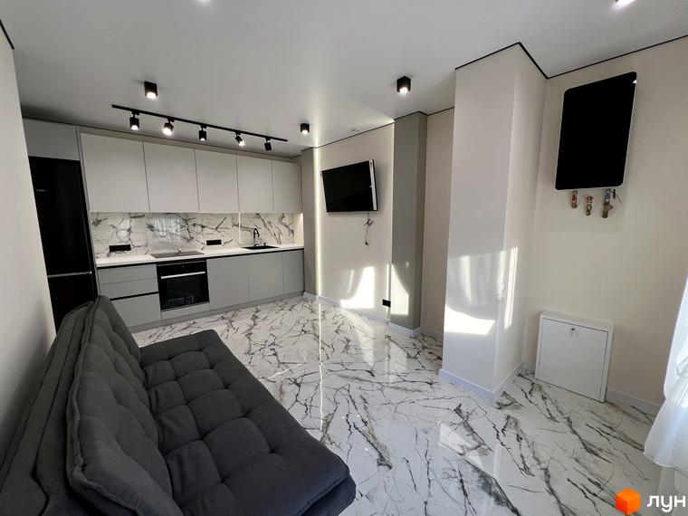 Інтер'єр квартири в клубному будинку Васильченка: сірий диван, сучасна кухня з мармуровим фартухом та білою стільницею, підлогою з мармуровою плиткою.