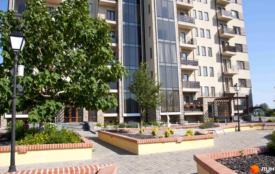 Житловий комплекс Premium Residence (Зелений Мис) з елегантним фасадом та скляним ліфтом. Навколо комплексу облаштована прибудинкова територія з ландшафтним дизайном та зонами відпочинку.