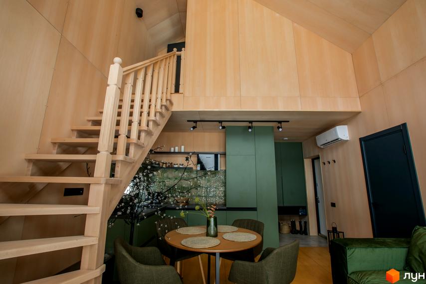 Інтер'єр котеджного комплексу КМ TYSHA: дерев'яні сходи, зелена кухня, обідня зона з кріслами та столом.