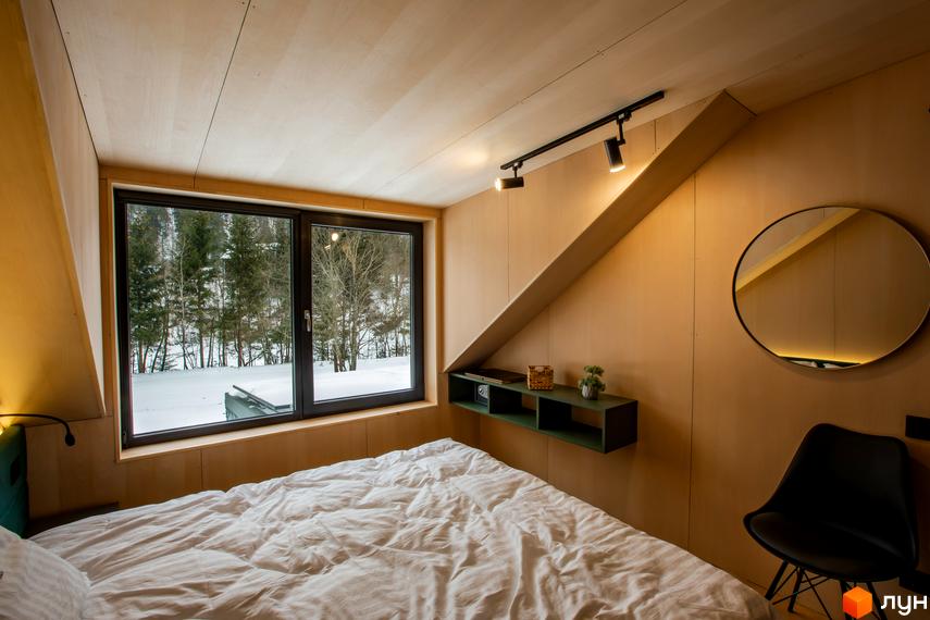 Затишна спальня в котеджному містечку КМ TYSHA з великим вікном, що виходить на зимовий ліс. Інтер'єр виконаний в натуральних дерев'яних тонах.