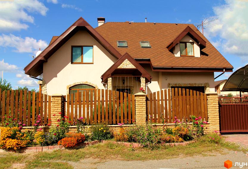 Зовнішній вигляд будинку КМ Лелечий Хутір з черепичною покрівлею та квітучим садом на прибудинковій території.