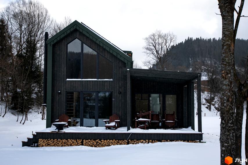 Котеджне містечко TYSHA: дерев'яний будинок з великими вікнами та терасою, оточений зимовим лісом та снігом.