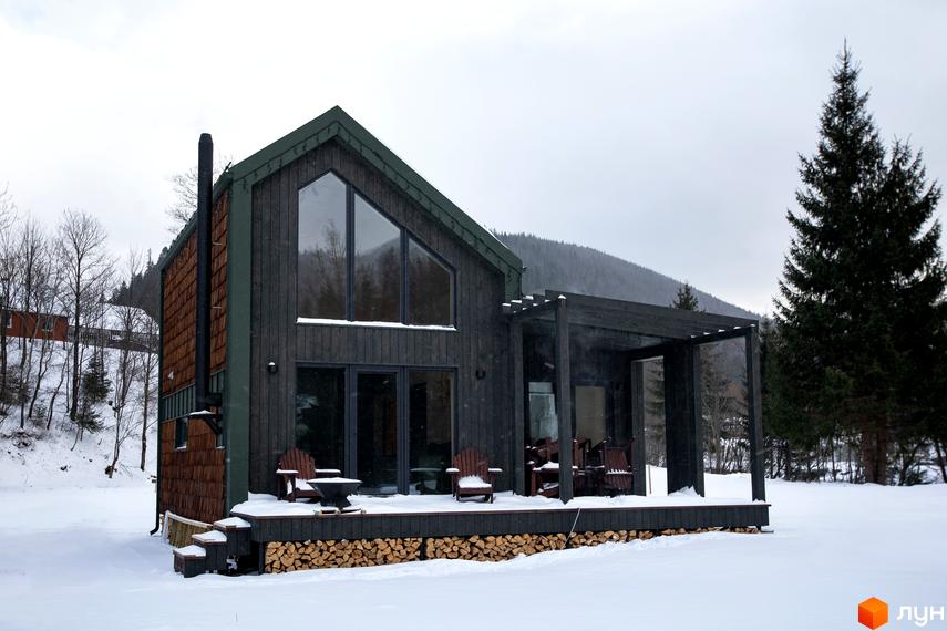 Котеджне містечко TYSHA у Карпатах взимку. Сучасний дерев'яний будинок з великими вікнами та терасою, оточений засніженим лісом.