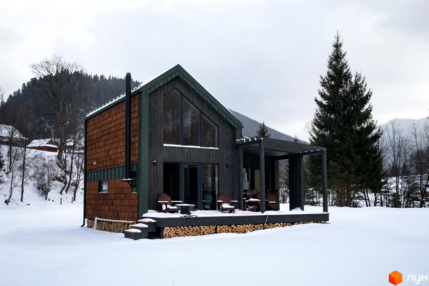 Котеджне містечко TYSHA: дерев'яний будинок з великими вікнами та терасою, оточений засніженим ландшафтом та ялинами.