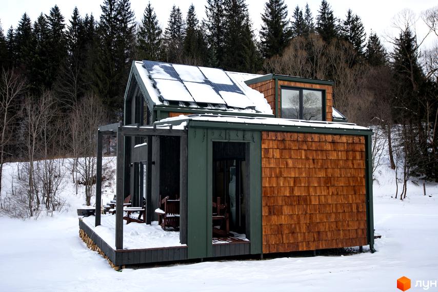 Котеджне містечко TYSHA взимку з дерев'яною обшивкою та сонячними панелями на даху, розташоване серед лісу.