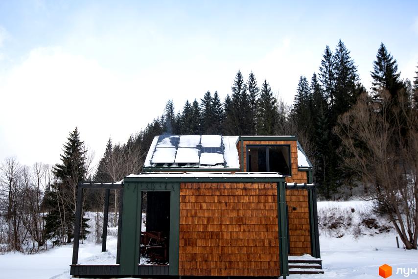 Котеджне містечко TYSHA взимку з дерев'яним фасадом та сонячними панелями на даху. Навколо будинку засніжена територія та ліс.