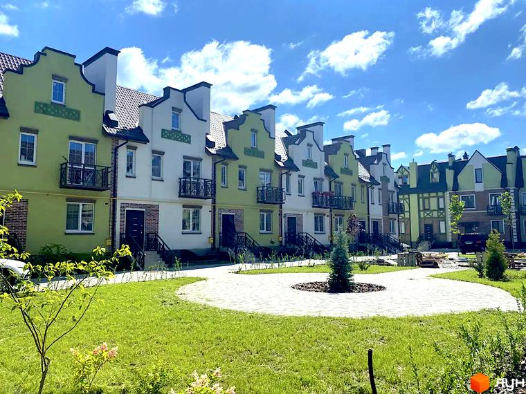 Ряд таунхаусів у Таунхауси „Нова Конча-Заспа“ із зеленими та білими фасадами, балконами та доріжками. На передньому плані зелений газон та вимощена доріжка.