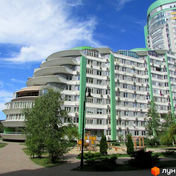 Багатоповерховий будинок Житлового комплексу Паркове місто з сірим фасадом та зеленими вставками, має вигнуті тераси. На передньому плані видно дитячий майданчик та зелені насадження.