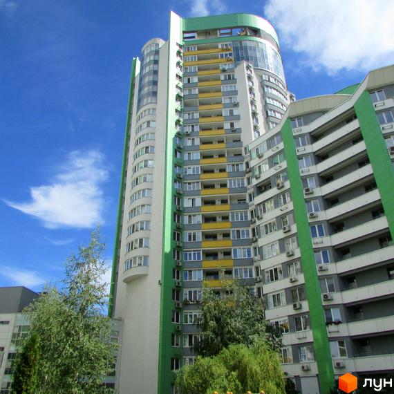 Високий житловий будинок Житлового комплексу Паркове місто з біло-зеленим фасадом та жовтими балконами. Навколо будинку ростуть зелені дерева та кущі.