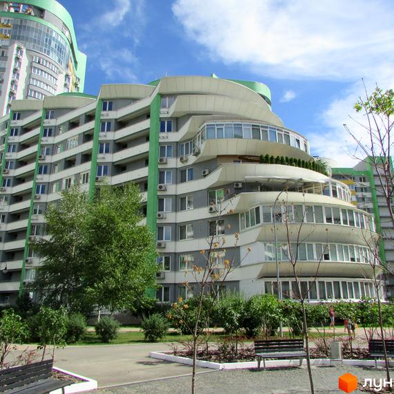 Житловий комплекс Паркове місто з багаторівневим фасадом, зеленими елементами та балконами. На прибудинковій території розташовані дерева, кущі та лавки.