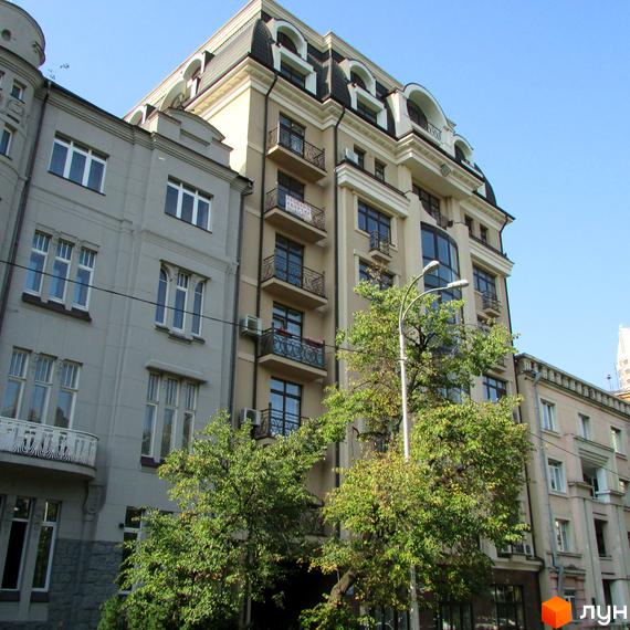 Житловий комплекс Botanic Paradise – світлий багатоквартирний будинок з мансардним дахом та балконами. Перед будівлею ростуть зелені дерева.