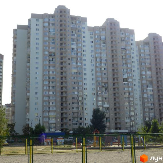 Житловий комплекс Троєщина з висотними будинками та прибудинковою територією, облаштованою дитячим майданчиком.