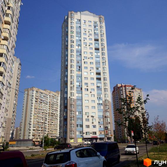 Житловий комплекс Троєщина, висотний будинок з великими вікнами та прибудинковою територією з зеленими насадженнями.