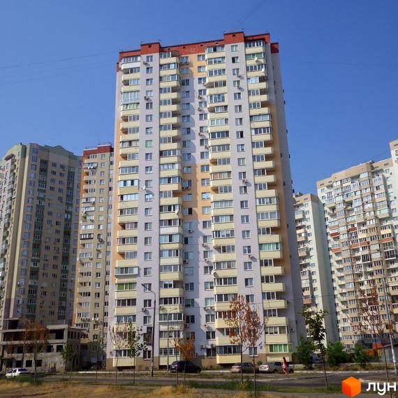 Житловий комплекс Троєщина з висотними будинками та прибудинковою територією. На фоні чисте небо та зелена зона.