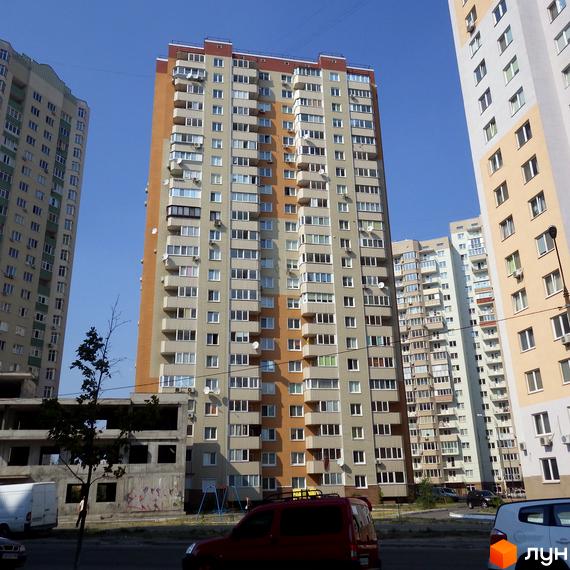 Житловий комплекс Троєщина з багатоповерховими будинками та прибудинковою територією. Вид на фасад будівлі з балконами та парковкою.