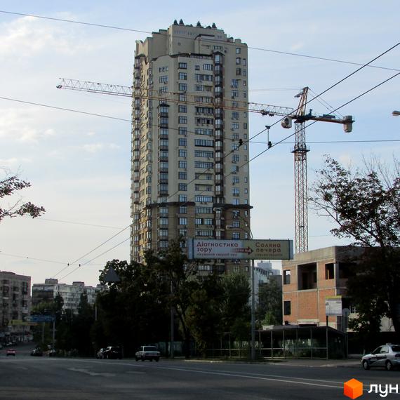 Житловий комплекс на вул. Солом'янська, 15а, висотний будинок з балконами та прибудинковою територією, що озеленена деревами.