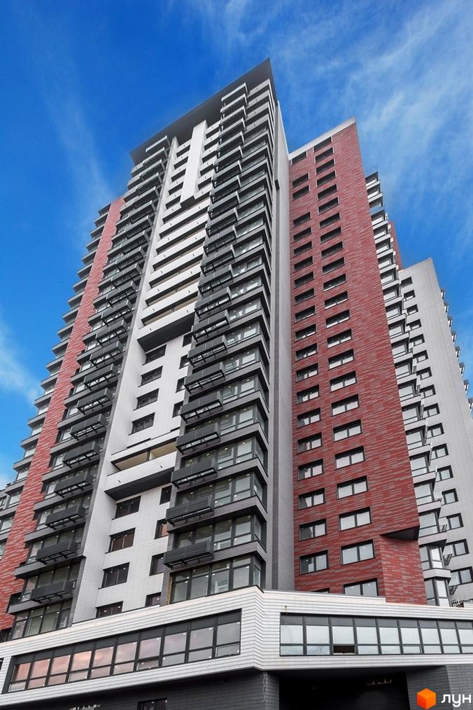 Висотна будівля ЖК West House з фасадом у сірих та червоних тонах на тлі блакитного неба. Багатоповерховий будинок з великою кількістю вікон та балконів.