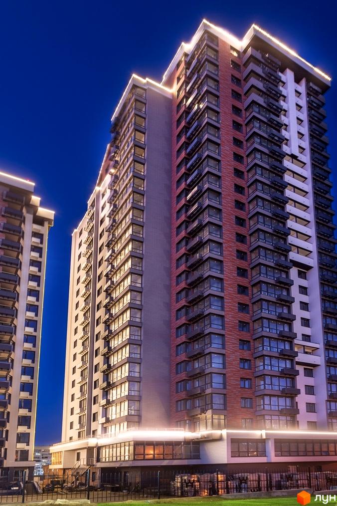 Висотна новобудова ЖК West House з панорамними вікнами та підсвічуванням фасаду на тлі вечірнього неба. На території комплексу є зелені насадження та огорожа.