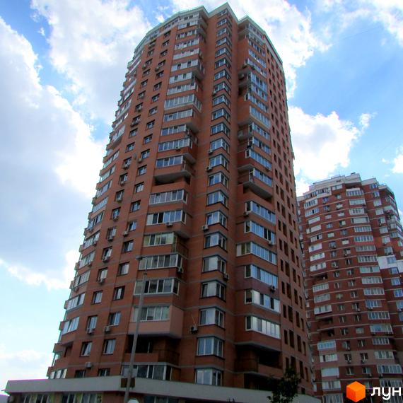 Вид на житловий комплекс з червоної цегли, висотні будинки з балконами та прибудинкова територія.