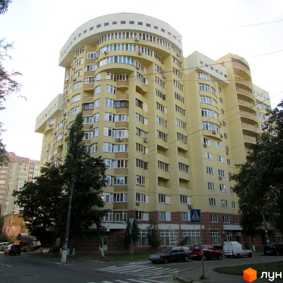 Житловий комплекс на вул. Васильченка, 3/24, з жовтою фасадною частиною та великими вікнами. Прибудинкова територія озеленена деревами та газонами.