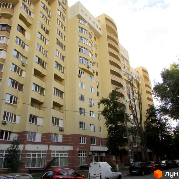 Житловий комплекс на вул. Васильченка, 3/24 з жовтою фасадною обробкою та великими вікнами. Прибудинкова територія озеленена деревами та автомобілями.