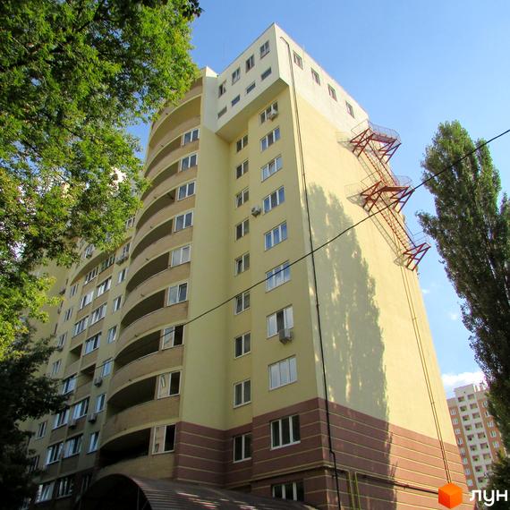 Житловий комплекс на вул. Васильченка, 3/24 з жовтою фасадною стіною та балконами. Прибудинкова територія з зеленими насадженнями.