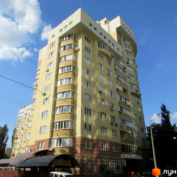 Житловий комплекс на вул. Васильченка, 3/24. Багатоповерховий будинок світло-жовтого кольору з коричневою нижньою частиною, численними вікнами та балконами. Навколо будинку дерева та частина прибудинкової території.