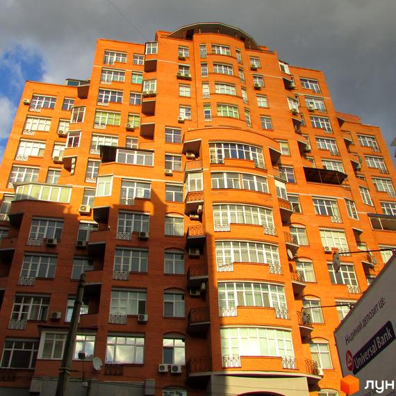 Житловий комплекс на вул. Дмитрівська, 66а, з червоною цегляною фасадою та великими вікнами. Прибудинкова територія облаштована для комфортного проживання.