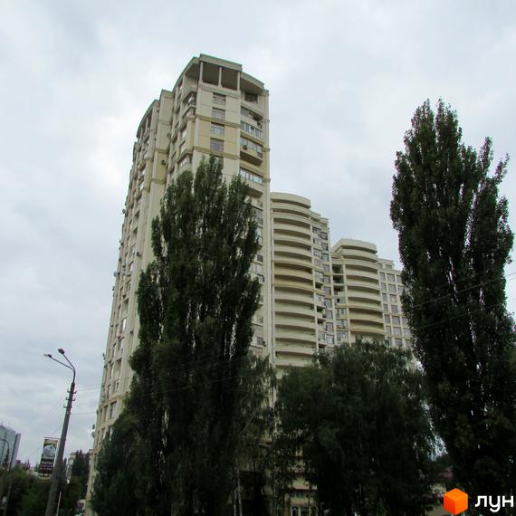 Багатоповерховий житловий комплекс Golden Park світлого кольору з вигнутими балконами. Перед будівлею ростуть високі дерева.