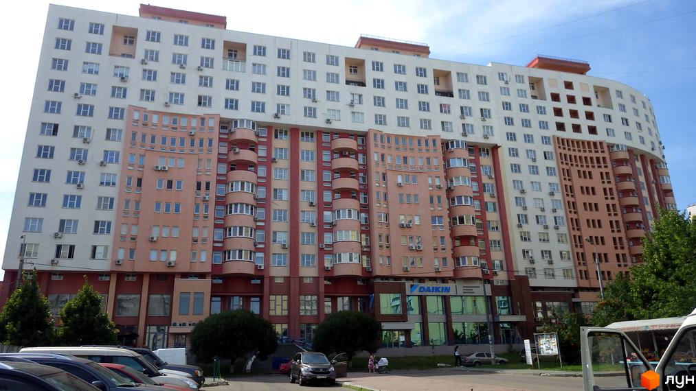 Житловий комплекс Перлина Кадетського Гаю: багатоповерховий будинок з білими, рожевими та коричневими фасадами, округлими балконами та комерційними приміщеннями на першому поверсі.